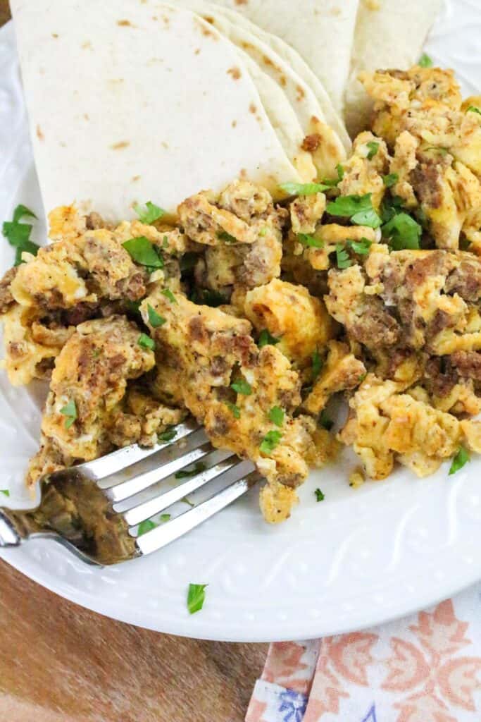 Chorizo and eggs on a white plate with a fork and chopped cilantro.