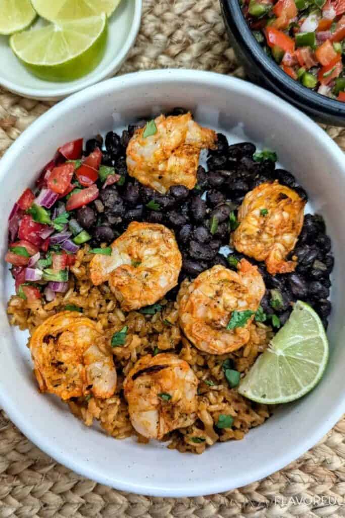 Shrimp with black beans, pico de gayo, and a lime wedge in a white bowl.