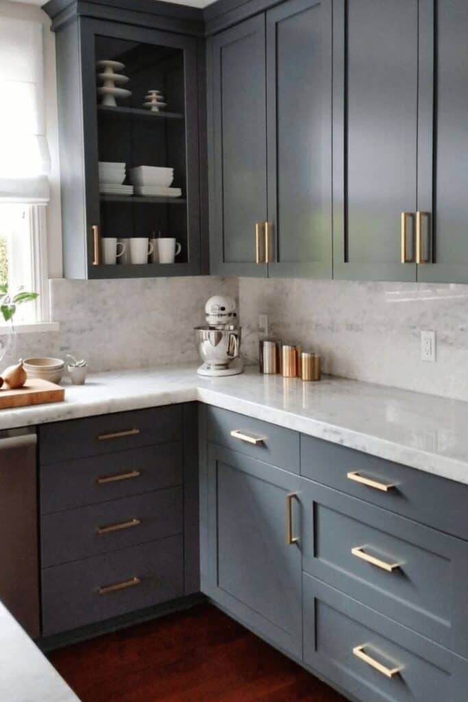 Dark gray kitchen cabinets with marble counters and backsplash and a stand mixer in the corner.