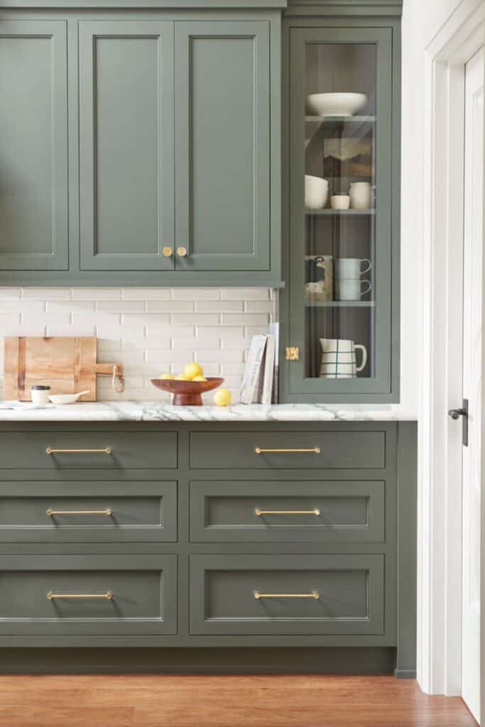 Sage green kitchen cabinets with gold hardware, marble counters, and a subway tile backsplash.