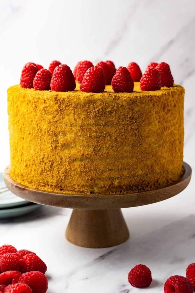 A cake on a wooden cake stand with raspberries on top.