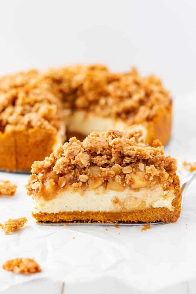 apple crumble cheesecake on a withe surface with a silver pie serving spoon.