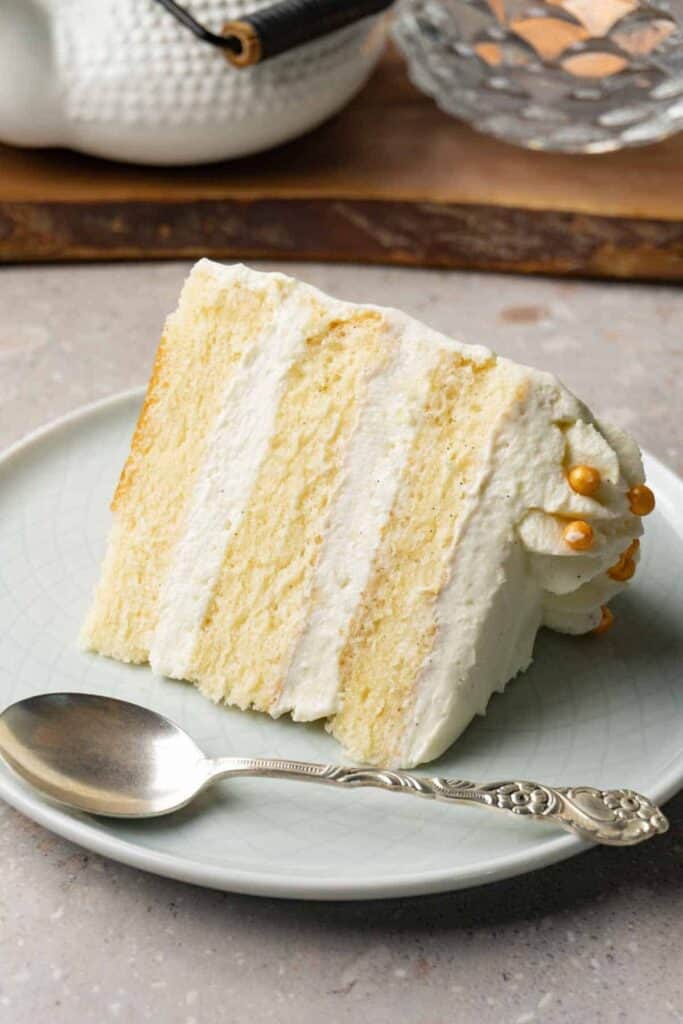 A vanilla cake with white icing on a light blue plate with a silver spoon.