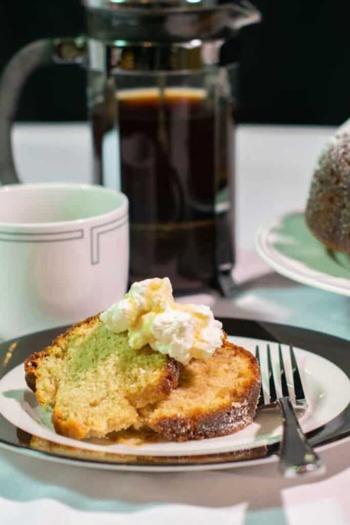 A slice of maple cinnamin bundt cake on a wite plate with a cup and pitcher of coffee in the background.