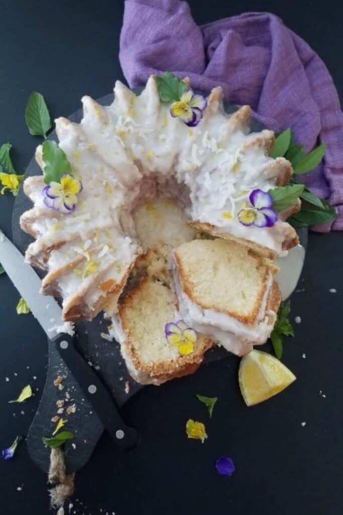 Lemon coconut pound cake on a white plate on a black surface with a purple napkin.