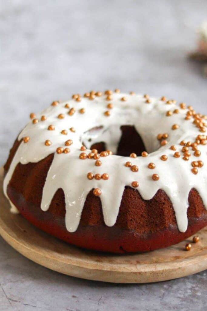 Red velvet bundt cake with white icing on a wooden plate.