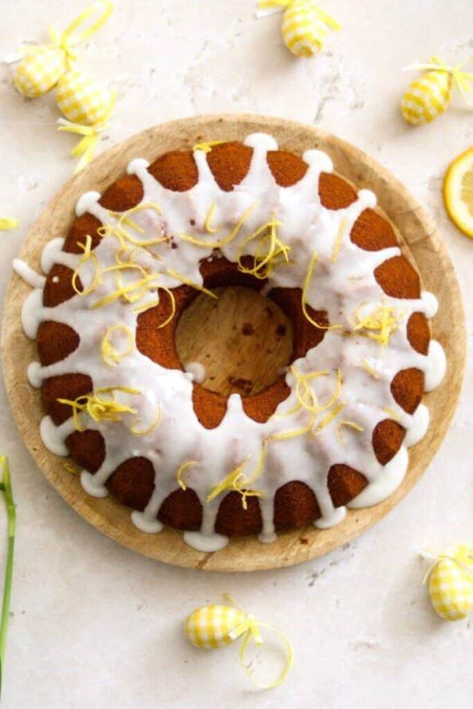 Lemon bundt cake with white icing and strips of lemon peel on a wooden plate.