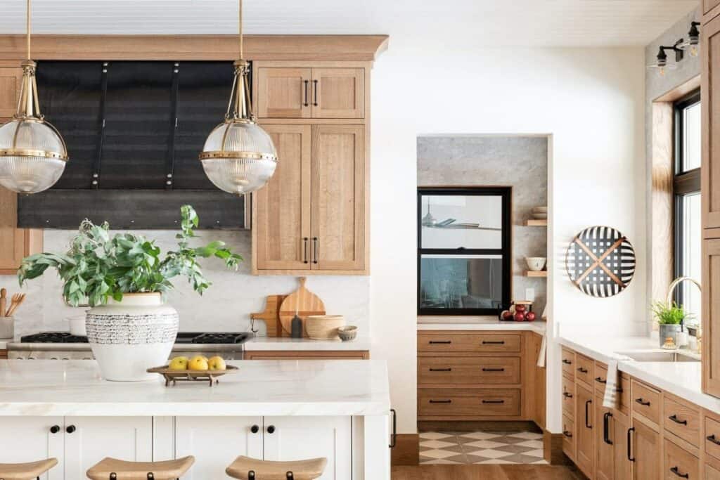 A kitchen with wood perimeter cabinets and a white island with a black vent hood and black hardware.