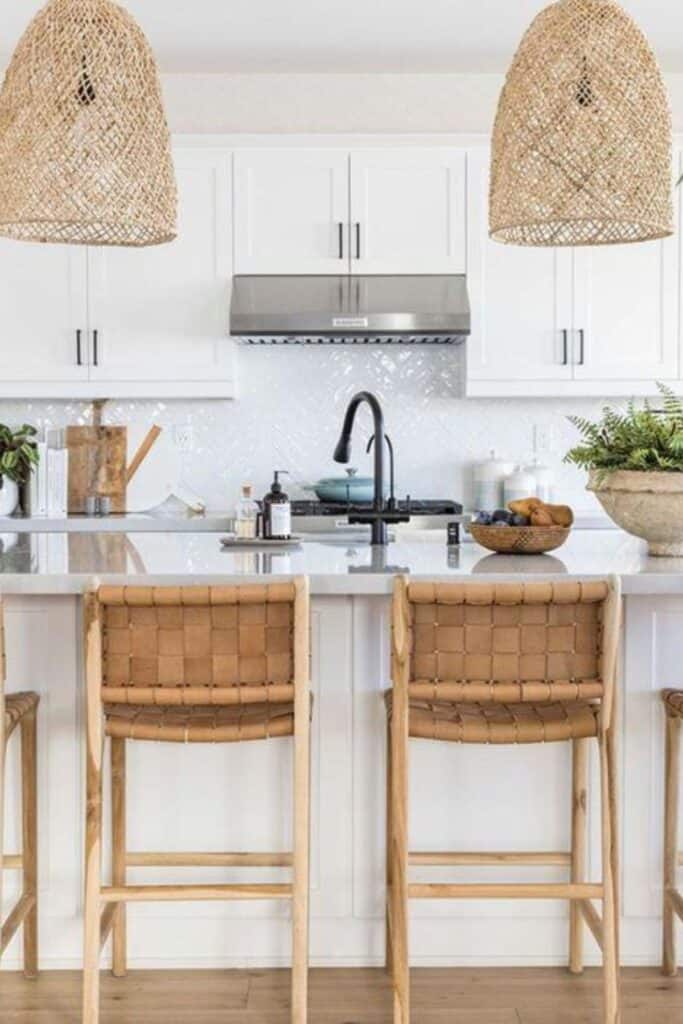 A white kitchen with white cabinets, white counters, woven pendent lights, leather woven bar stools and black hardware.