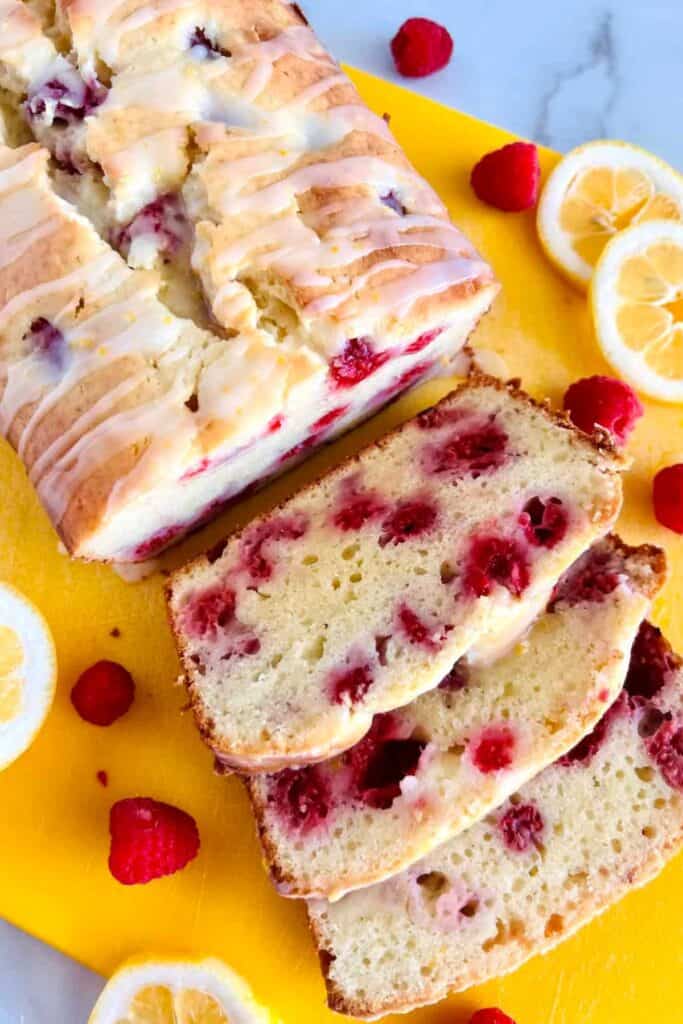 Raspberry lemon loaf on a yellow cutting board with raspberries and sliced lemons.
