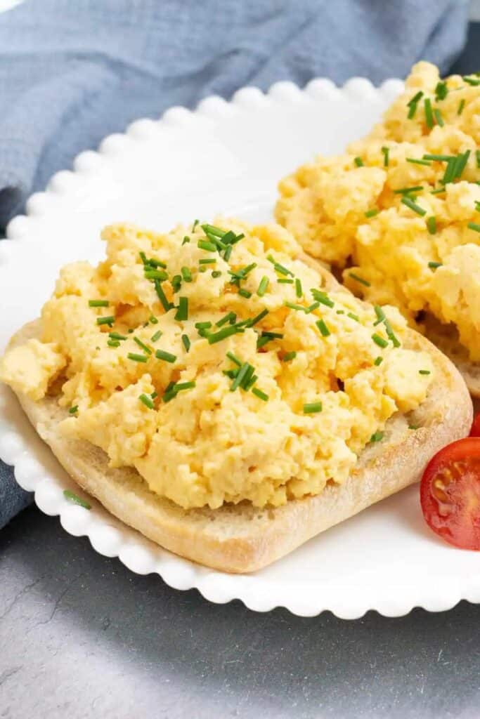 fluffy ricotta scrambled eggs with chives on a piece of bread on a white plate.
