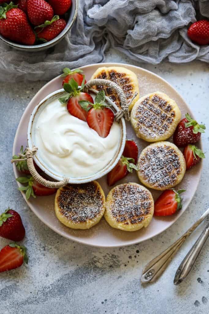 cottage cheese pancakes on a white plate with sliced strawberries and a bowl with a white dip.