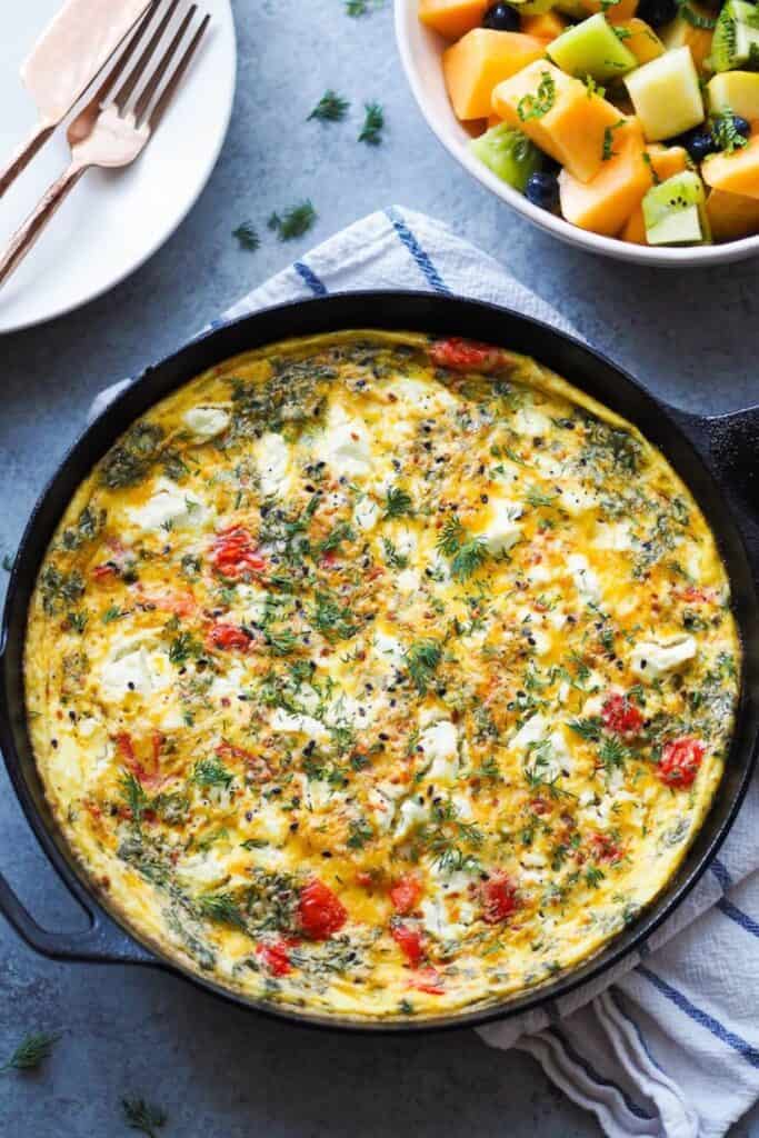 Everything Bagel Fritatta in a cast iron pan on a dish towel that is white with blue stripes.