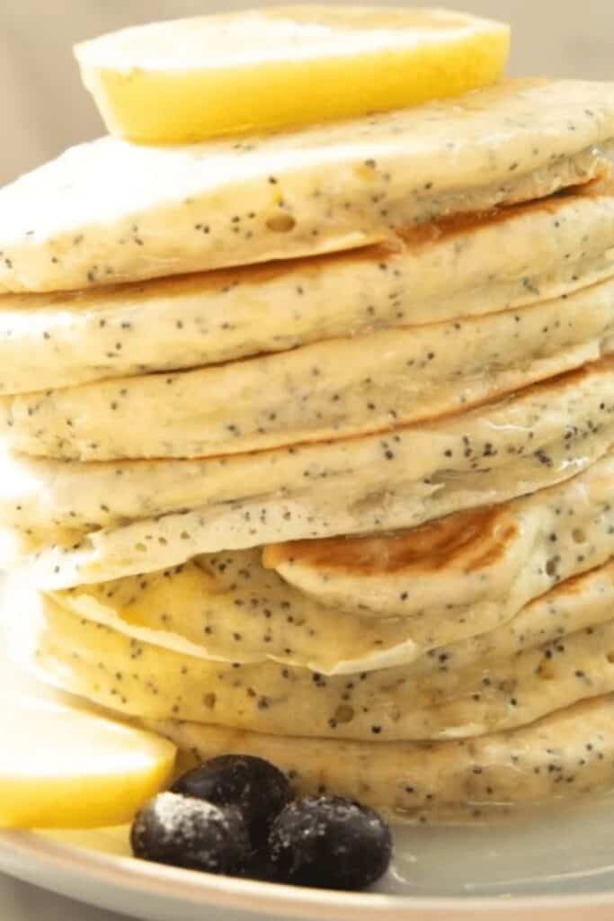 lemon poppyseed pancakes stacked on a white plate with blueberries and lemon sices.