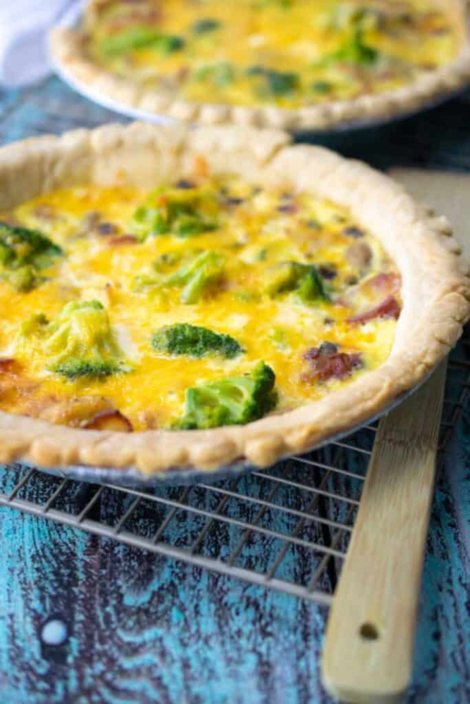 Quiche in a metal pie plate on a cooling rack.