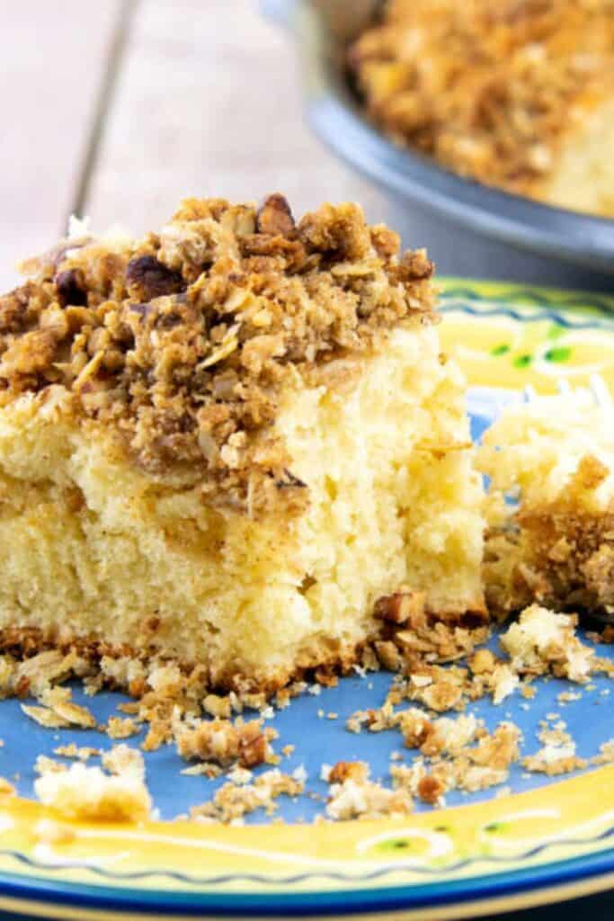 A piece of cinnamin strussel coffee cake on a blue and yellow plate with lots of crumbles all around. 