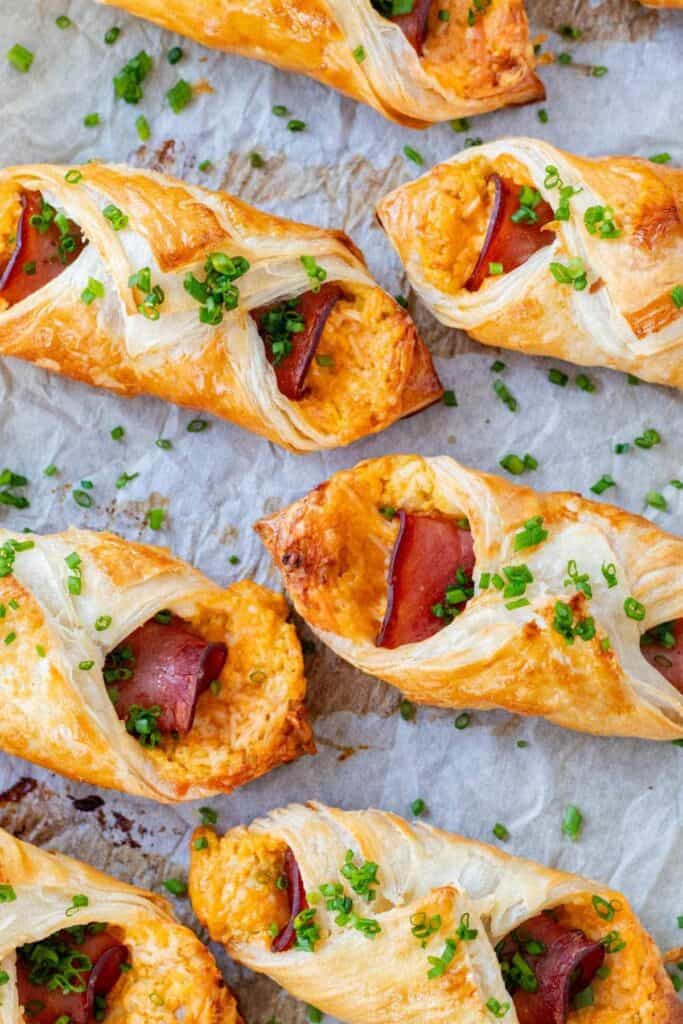 ham and cheese in a puffed pastry that is on a piece of parchment paper with sliced scallions all over.