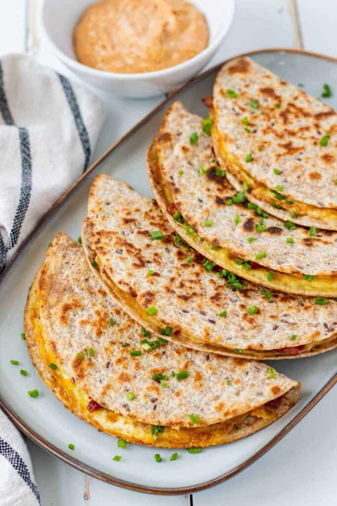 smashed breakfast egg tacos on a light blue platter sprinkled with scalions with a white bowl of a sauce and a striped towl next to the platter.