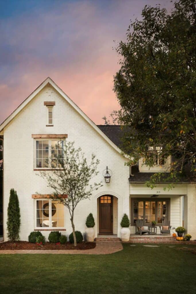 The exterior of a tudor home with a tall peak on the left, painted brick in Oyster White and an arched doorway.