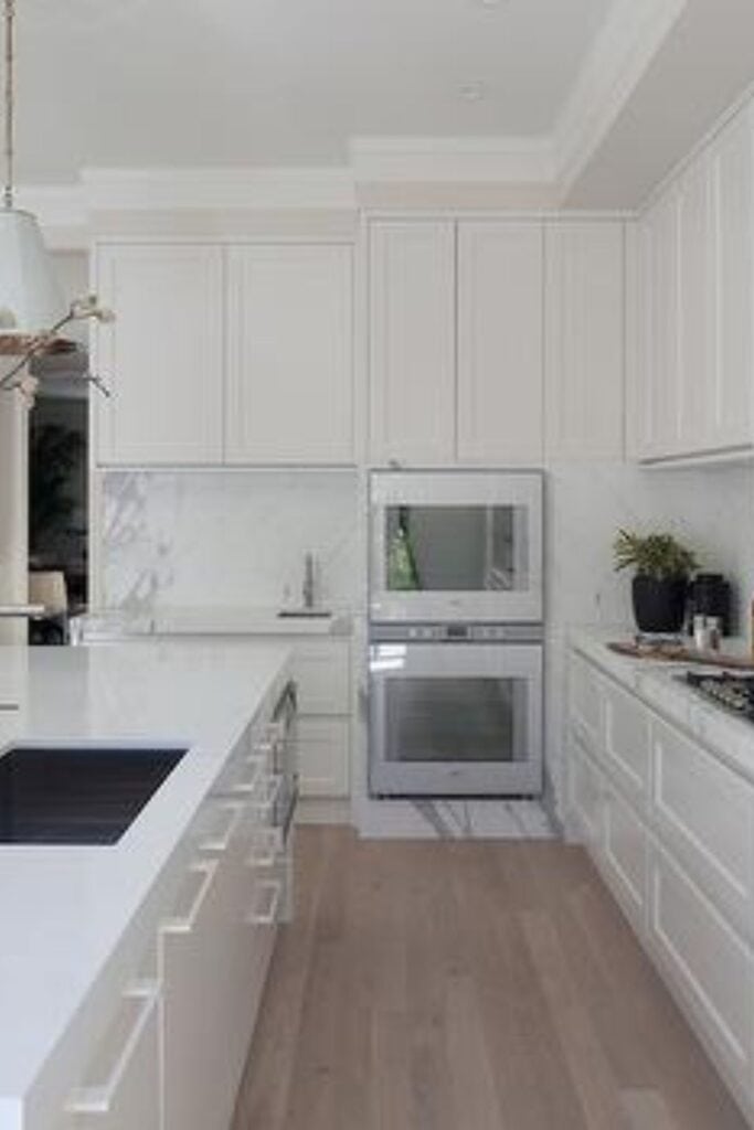 A kitchen with cabinets painted in Ballet White, white appliances and marble counters and backsplash.