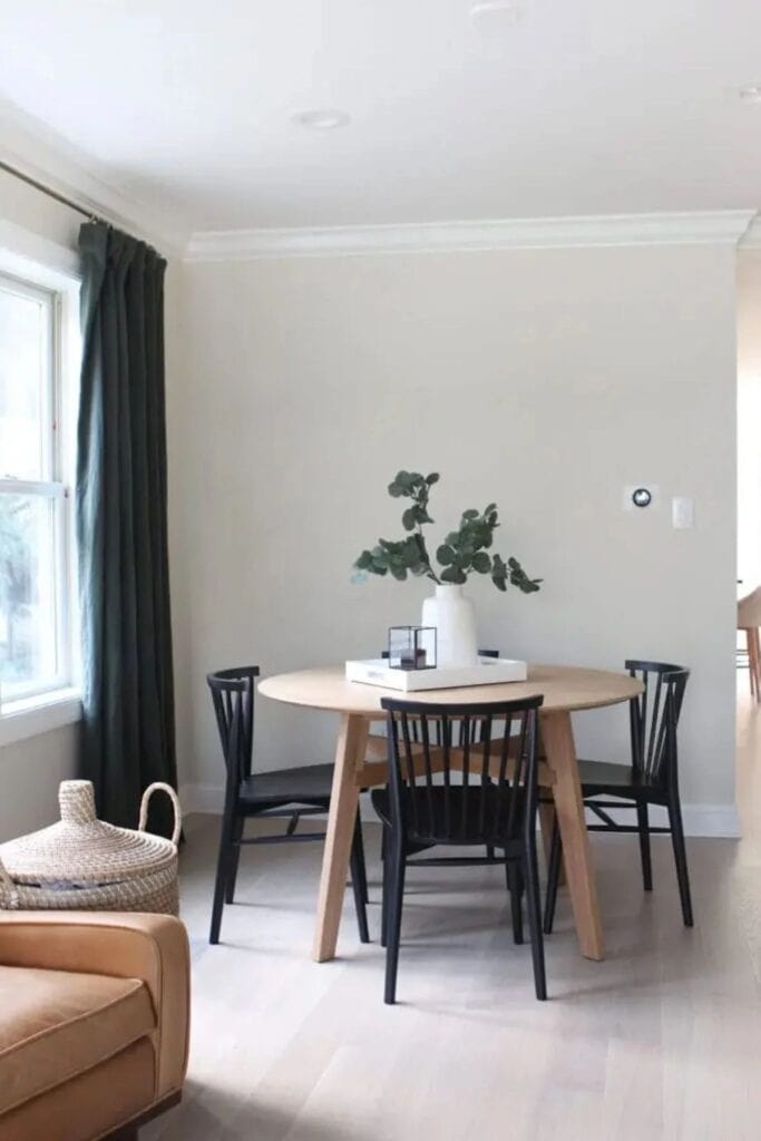 A dining space with a wood table and black chairs, the walls in Ballet White, and black curtains.