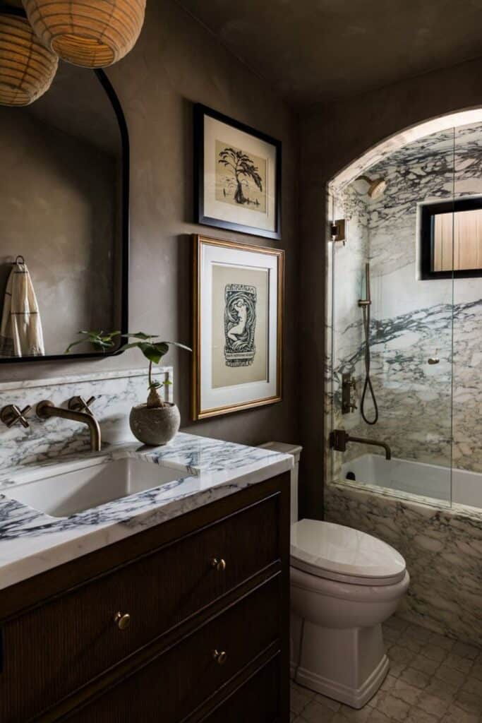 A black bathroom with a marble shower and counter with an arched mirror.