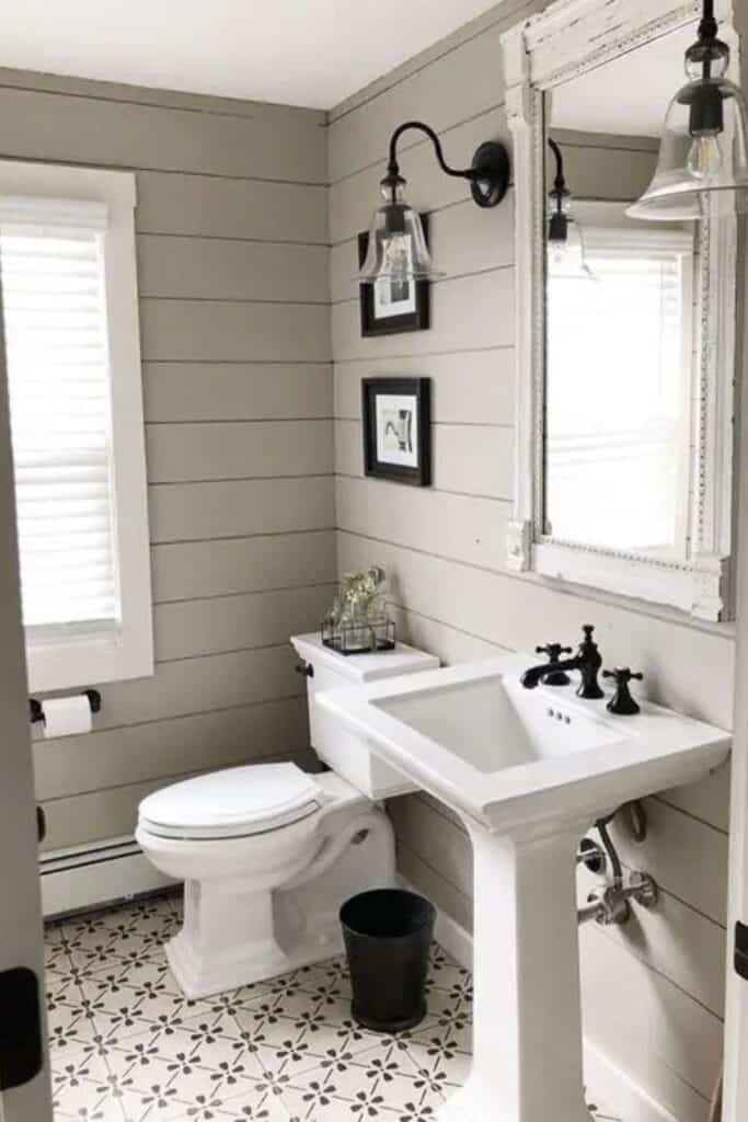 A bathroom with greige shiplap, a patterned tile floor and black hardware with a pedestal sink.