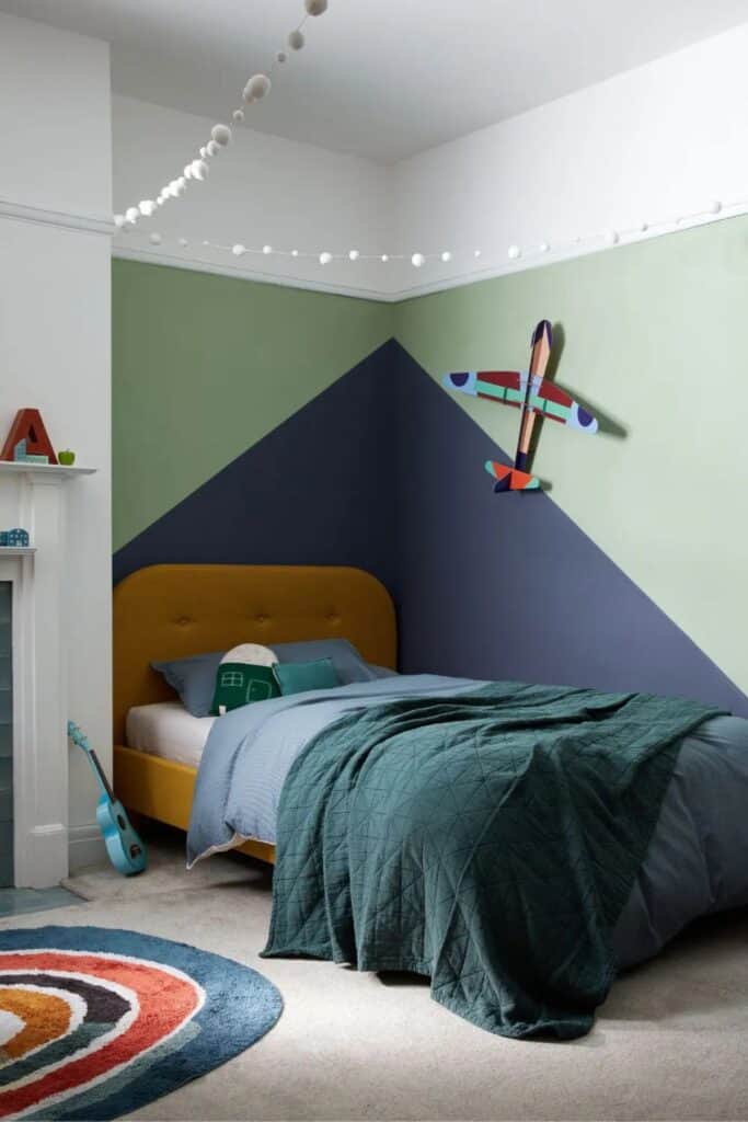 A boys room with color blocking walls that are navy and sage with an airplane on the wall.