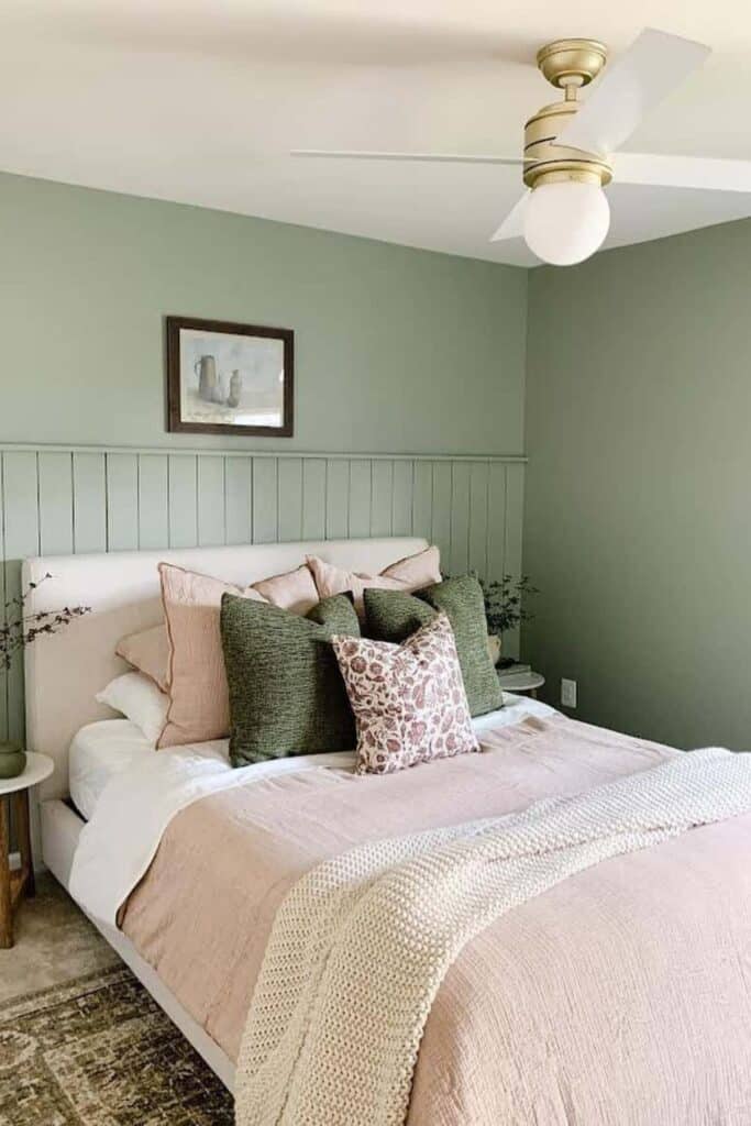 A bedroom with sage green walls and the bed has pink bedding with dark green throw pillows.
