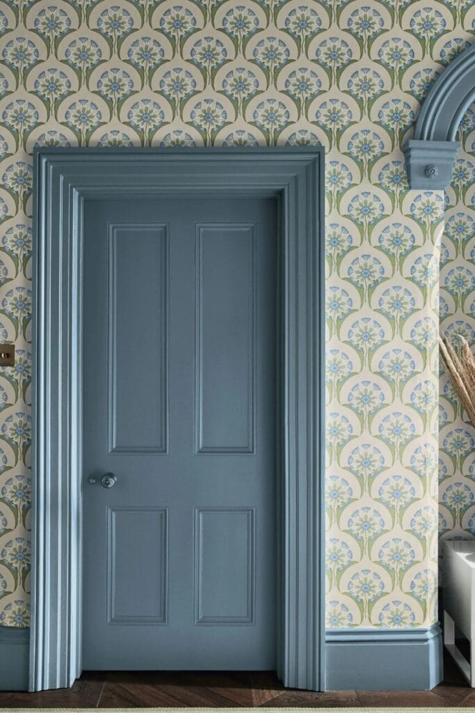 A wall with a door painted dusty blue with wallpaper that is white, sage gree, and dusty blue.