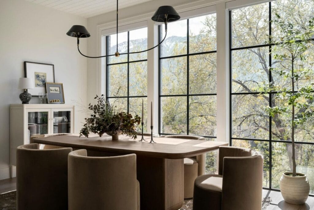 A wood dining table with curved upholstered chairs and a large wall of windows looking on to nature.