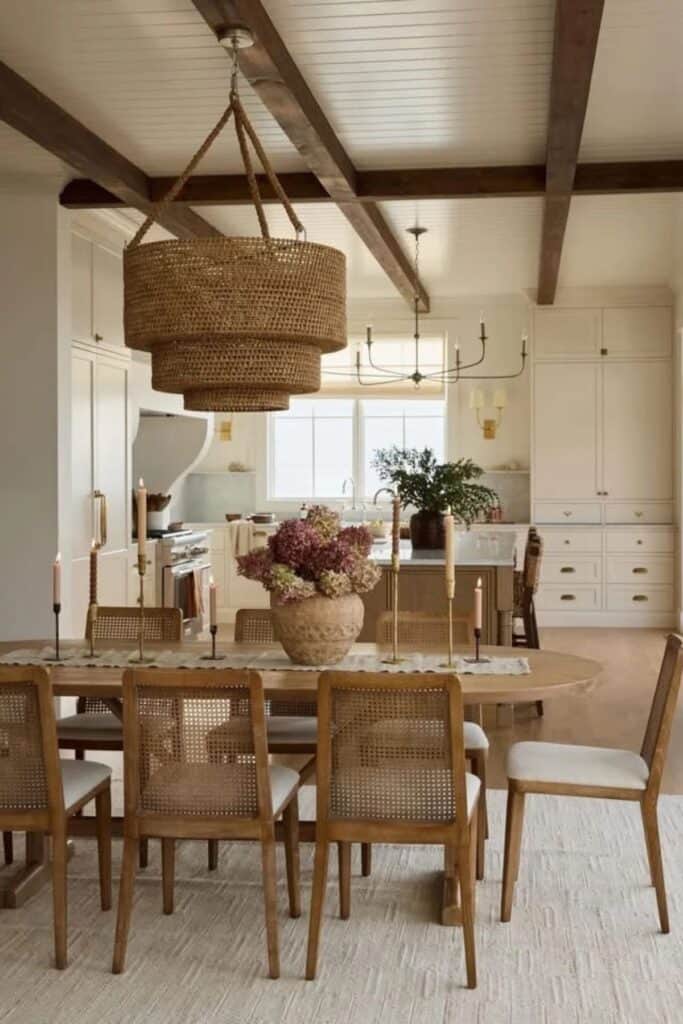 A dining room with an oval wood table, a huge woven light fixture and a kitchen in the background with a large metal chandelier.