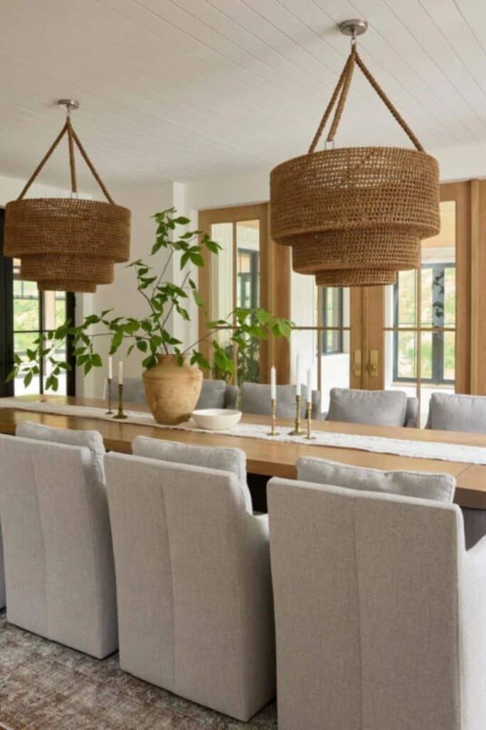 A dining table with gray upholstered chairs and two woven light fixtures.