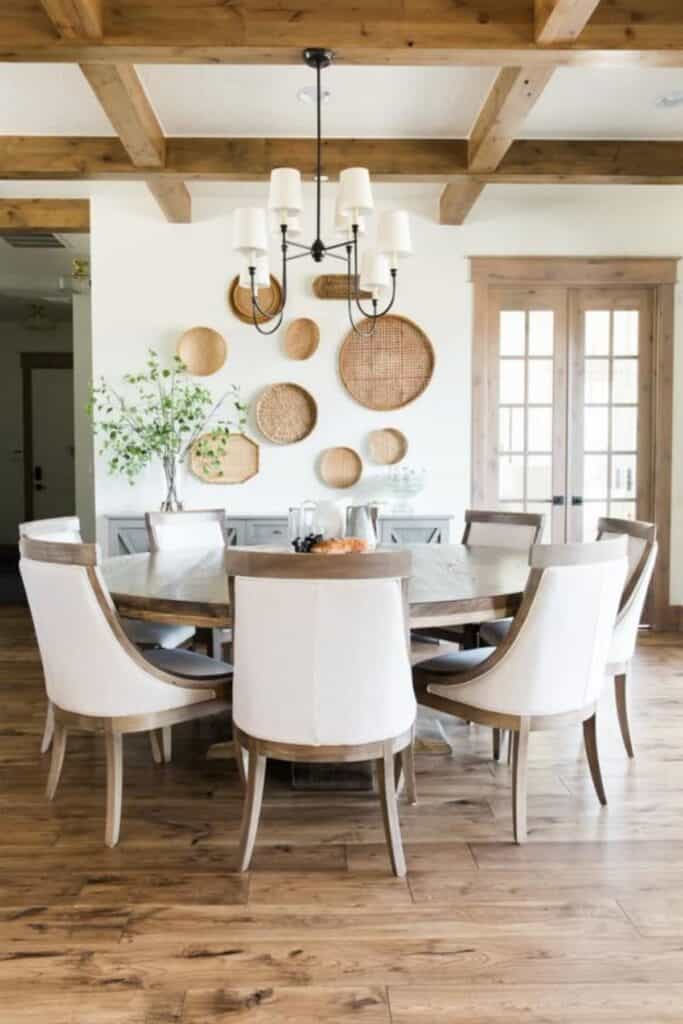 A round dining table with white upholstered chairs with wood trim, wood floors, and wood cased french doors.