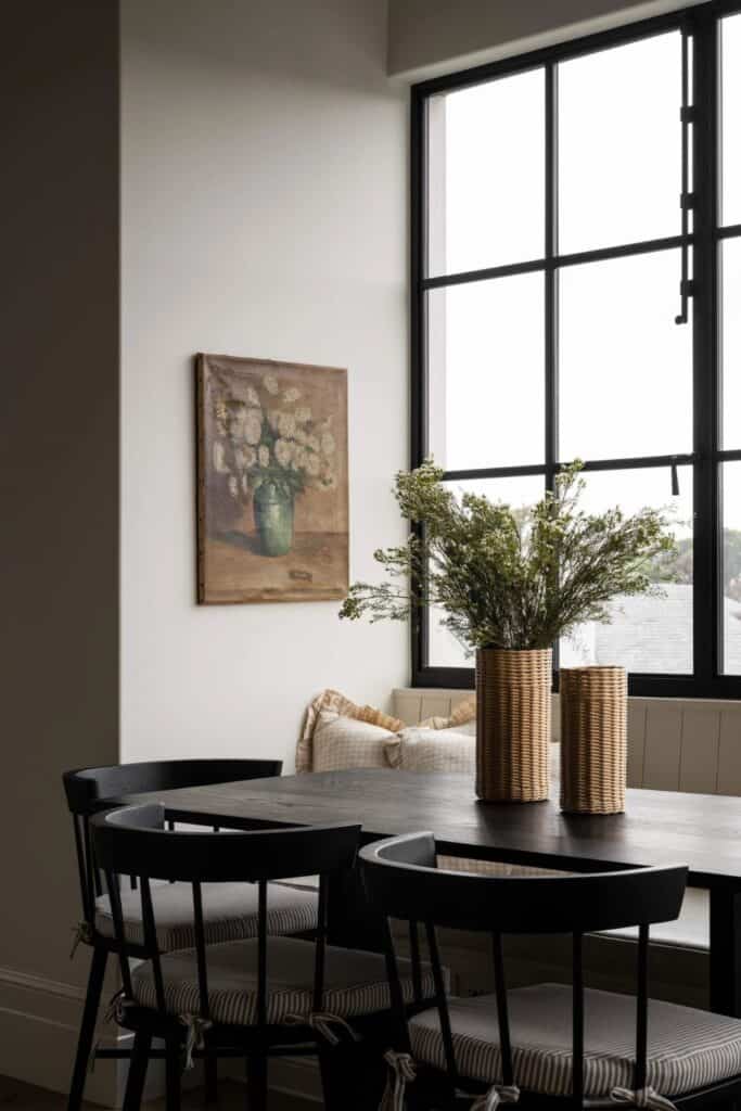 A black wood table and black chairs with a bench on one side and a wall of black windows above.