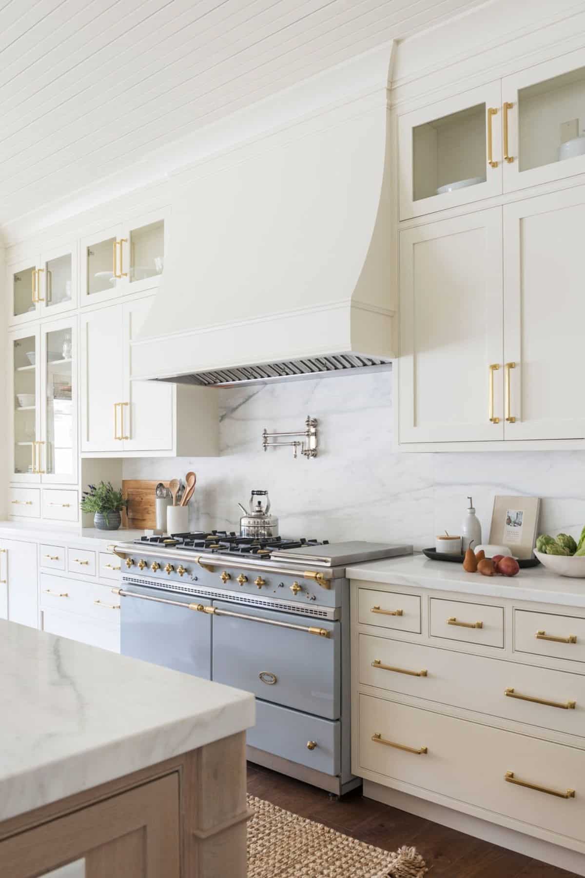 A cream kitchen with gold hardware and cabinets with glass doors above the upper cabinets.