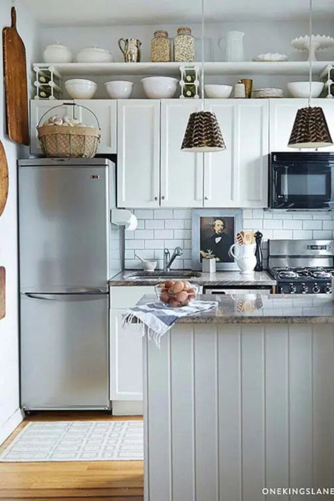 A hwite kitchen with an additional shelf above the upper cabinets with whtie mixing bowls, cake stands, and jars of beans on them.