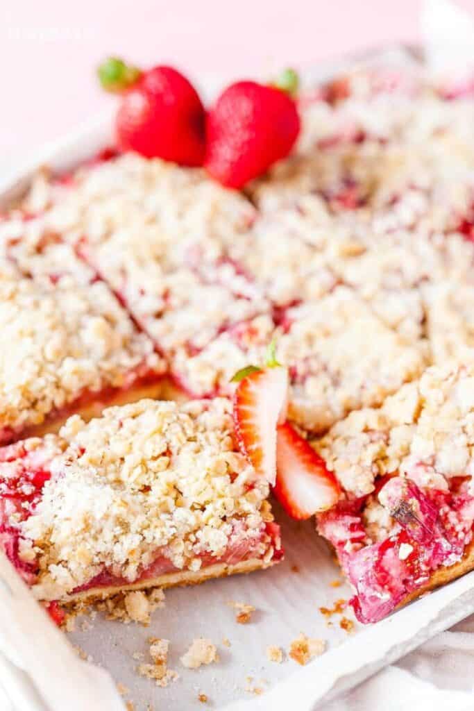 Strawberry rhubarb bars sliced in a white dish with strawberry garnish.