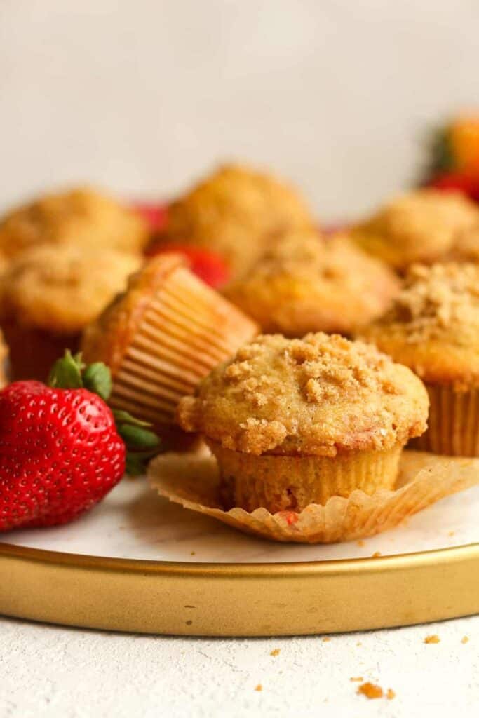 Strawberry rhubarb strussel muffins with paper liners on a gold tray with strawberries.