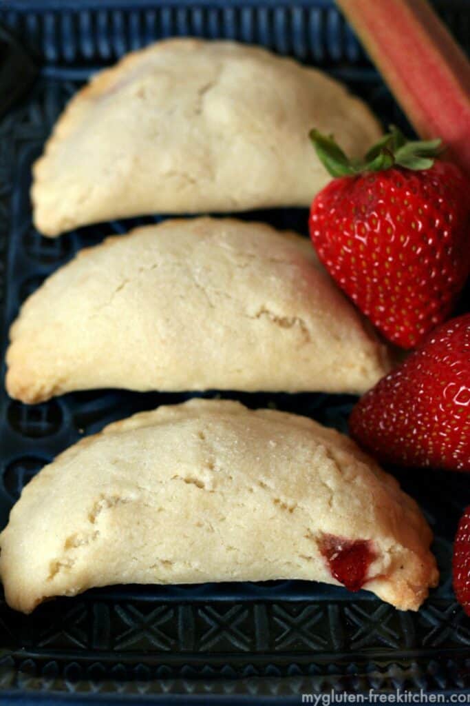 strawberry rhubarb hand pies on a black plate with strawberries.