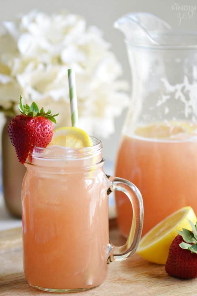 A strawberry rhubarb lemonade in a mason jar with a lemon and strawberry garnish.