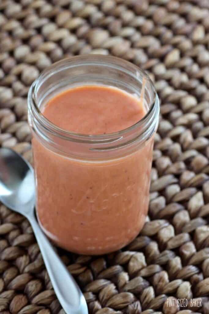 Strawberry rhubarb curd in a mason jar with a silver spoon next to it on a woven placemat.