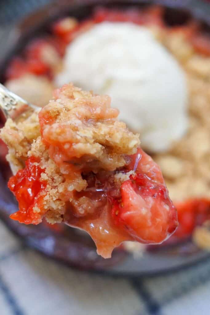 Strawberry rhubarb crisp on a silver spoon.