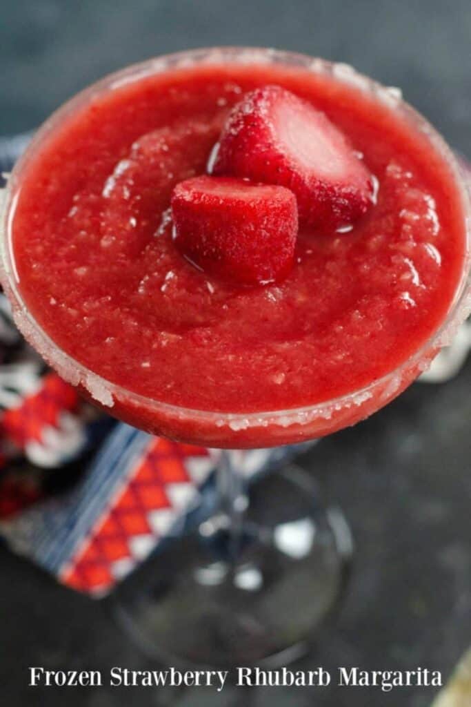 frozen strawberry rhubarb margarita with salt on the rim with strawberries as a garnish.