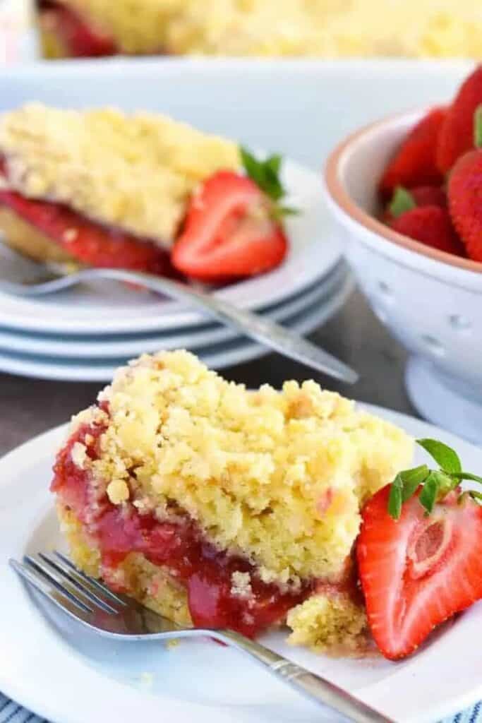 A slice of strawberry rhubarb coffee cake on a white plate with a silver fork.