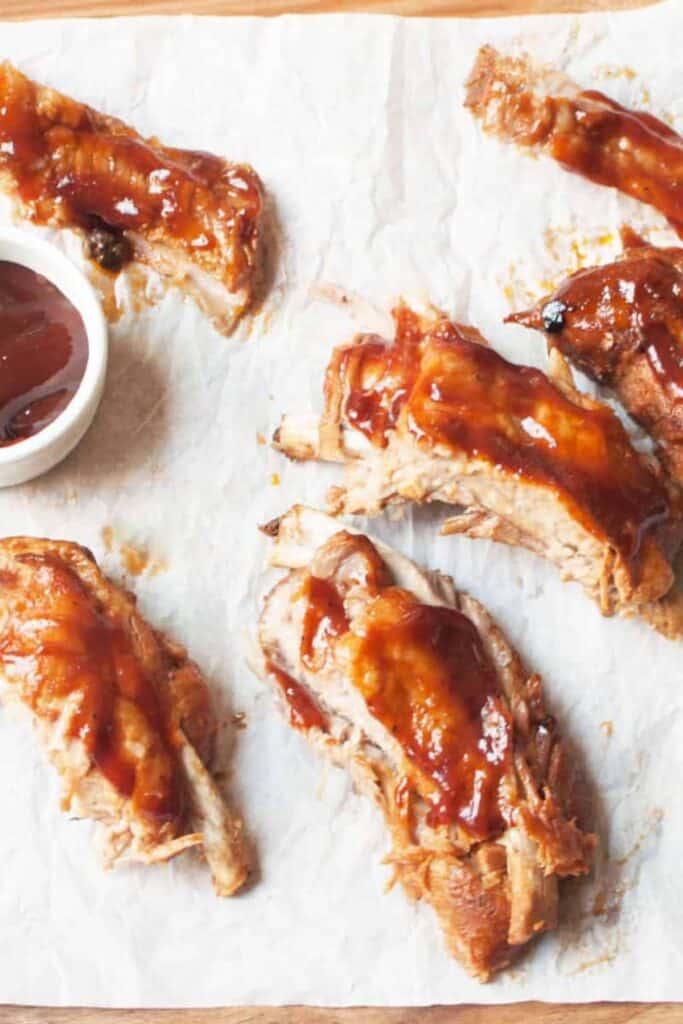 Rootbeer Ribs on a white piece of parchment and a ramekin of barbeque sauce.
