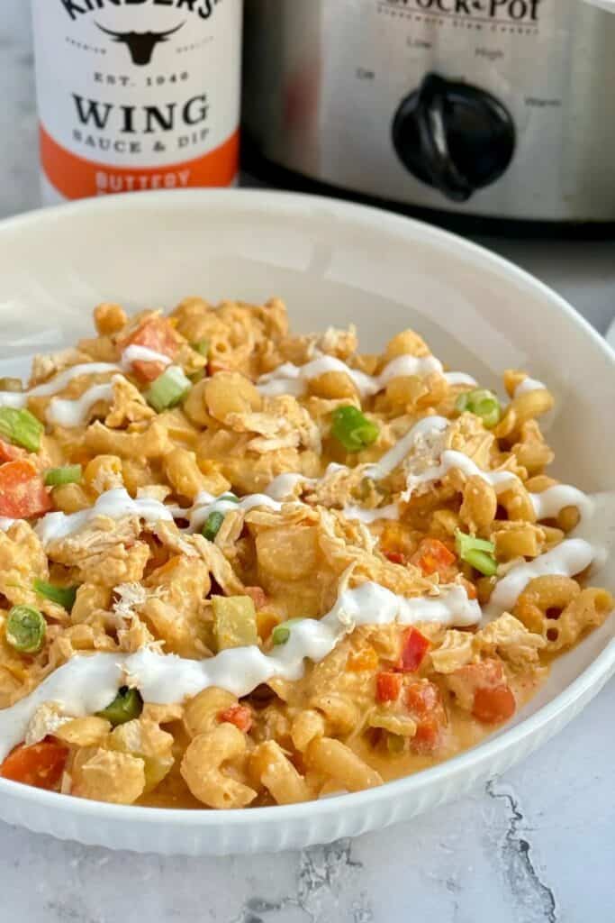 buffalo chicken pasta on a white plate with chives and a cream sauce on top.