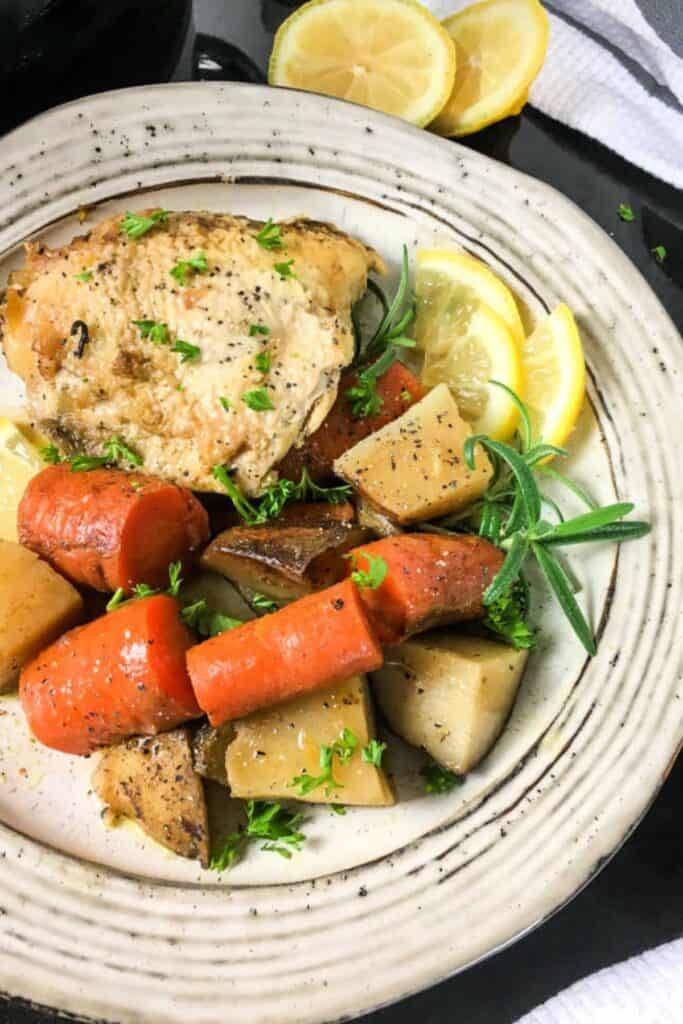 rosemary lemon chicken thights with potatoes and carrots with a sprig of rosemary, lemon wedges on a white plate.