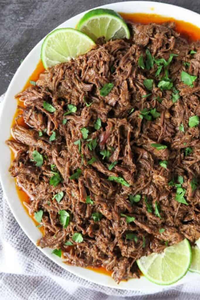 mexican shredded beef on a white plate with lime wedge and sprikled parsley.