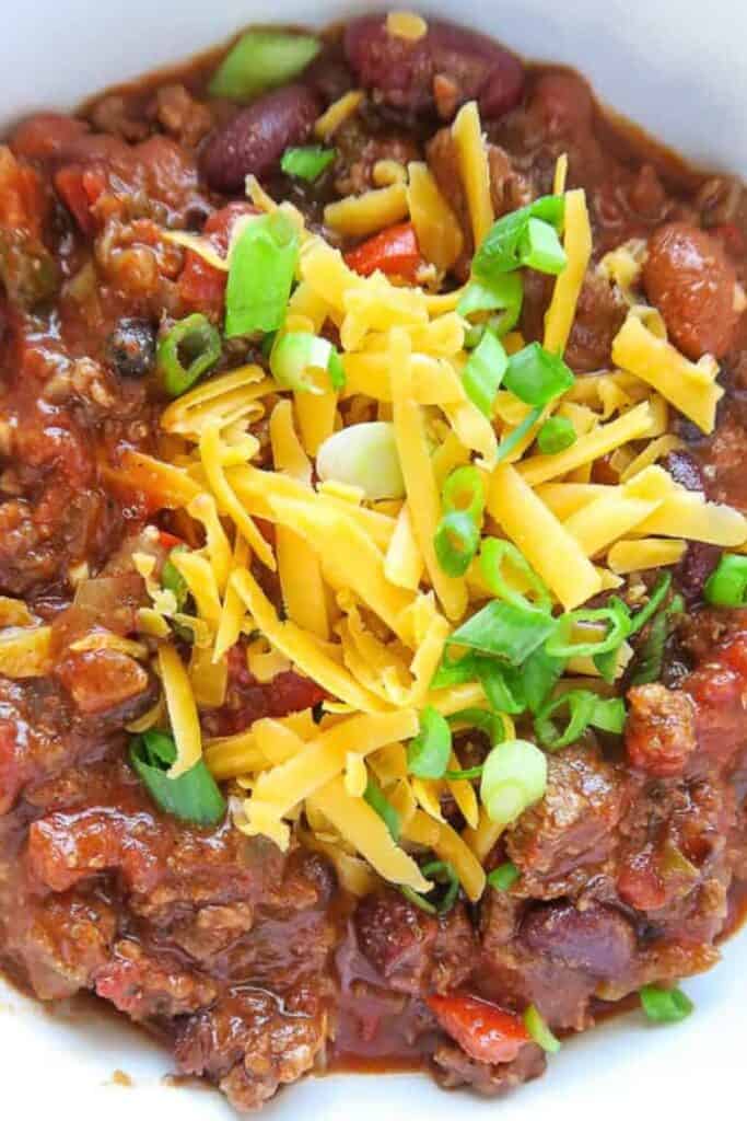slow cooker chili with cheese and green onions on top.